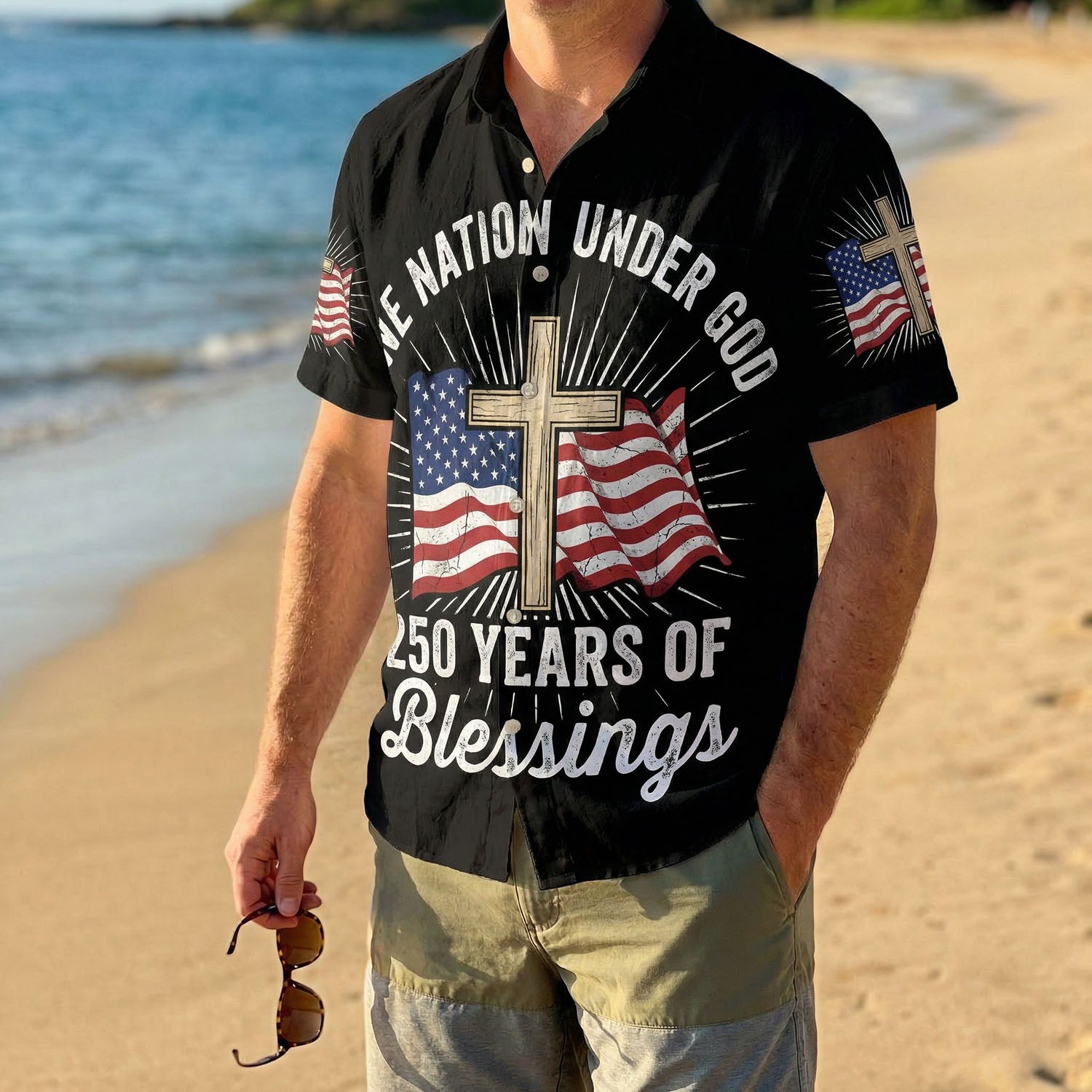 A male model wearing the black One Nation Under God Aloha shirt on a sunny beach, showcasing a comfortable summer holiday style.