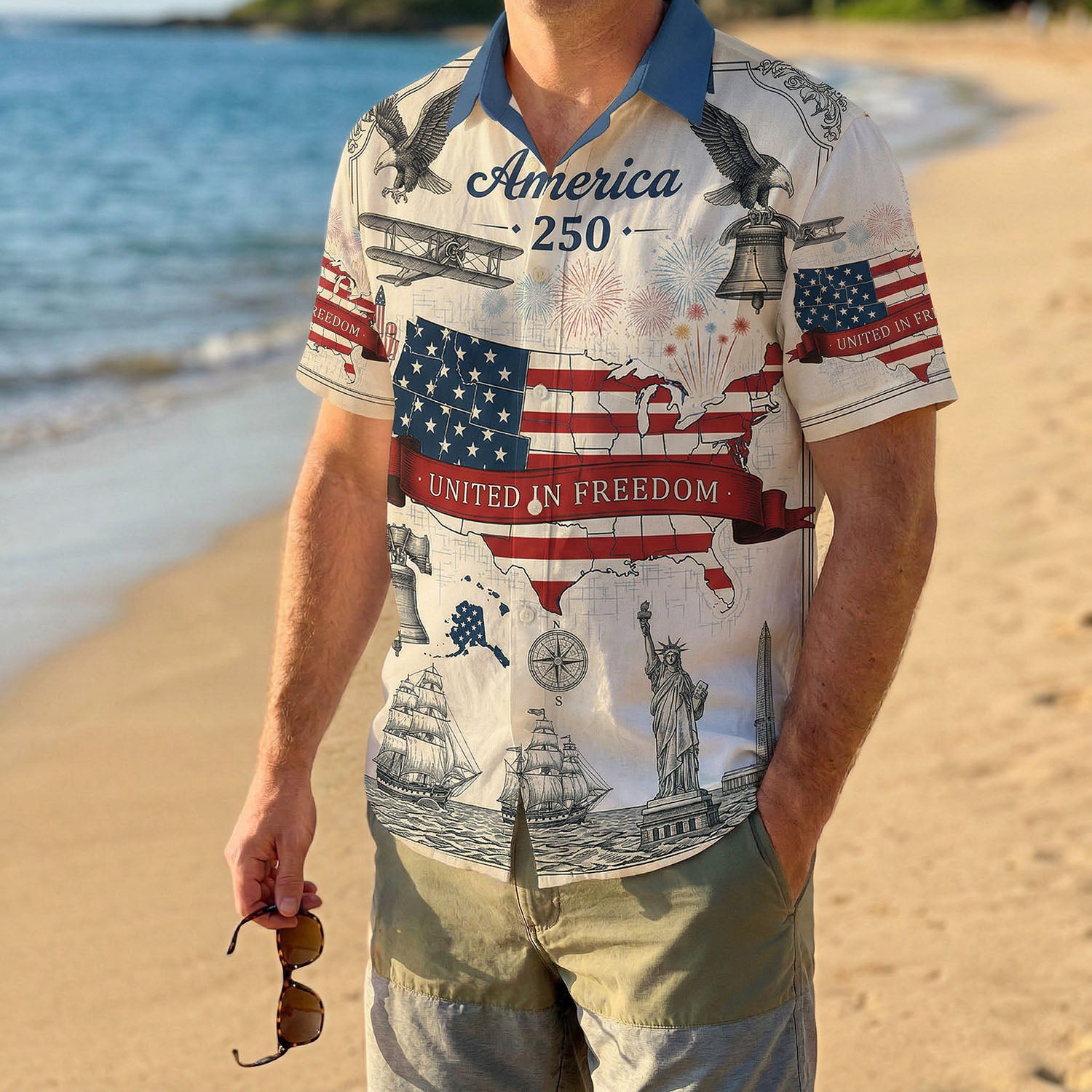 A male model wearing the vintage America 250 United In Freedom shirt on a sunny beach showcasing a casual patriotic summer outfit