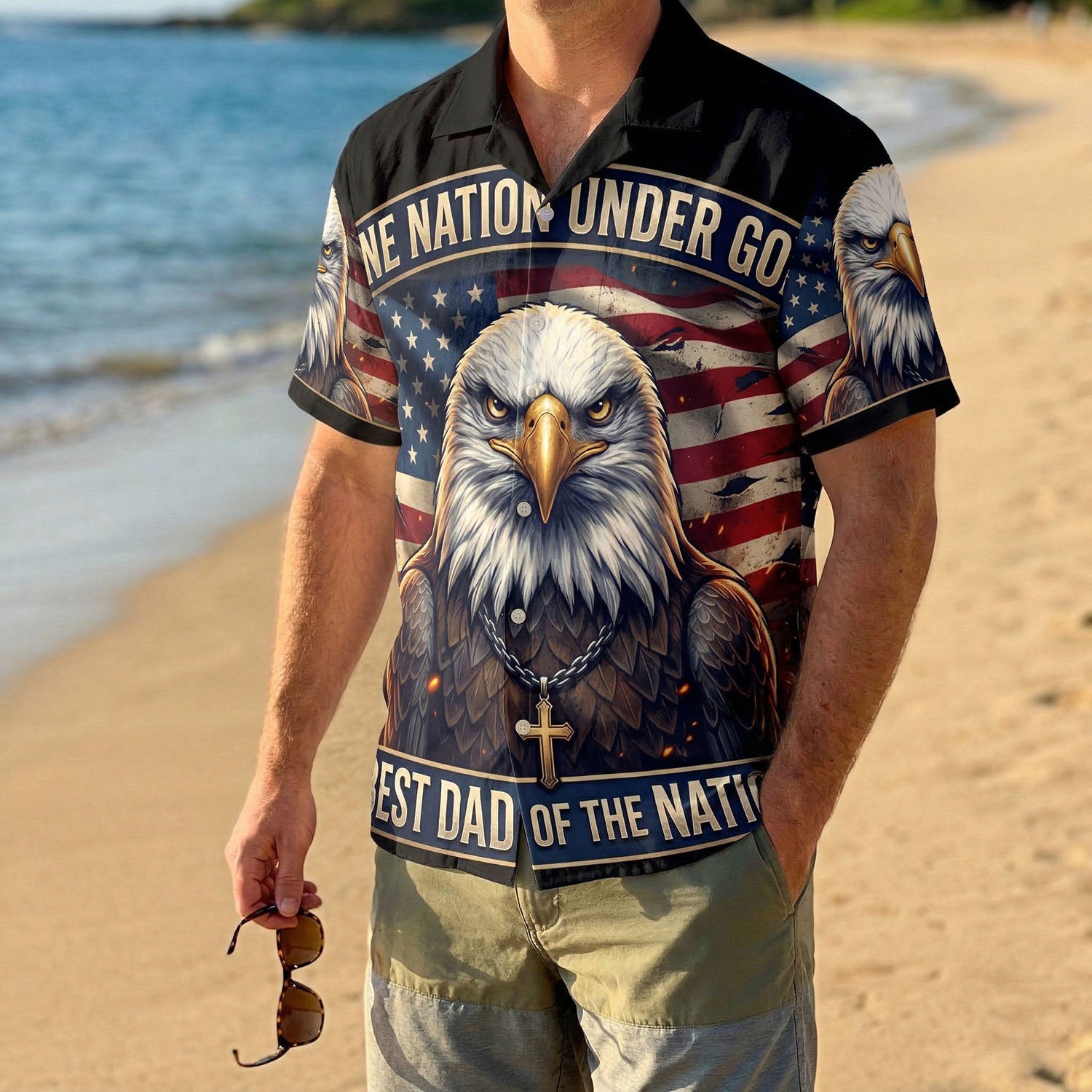 A male model wearing the black One Nation Under God religious shirt on a sunny beach showcasing a patriotic Father's Day summer gift look