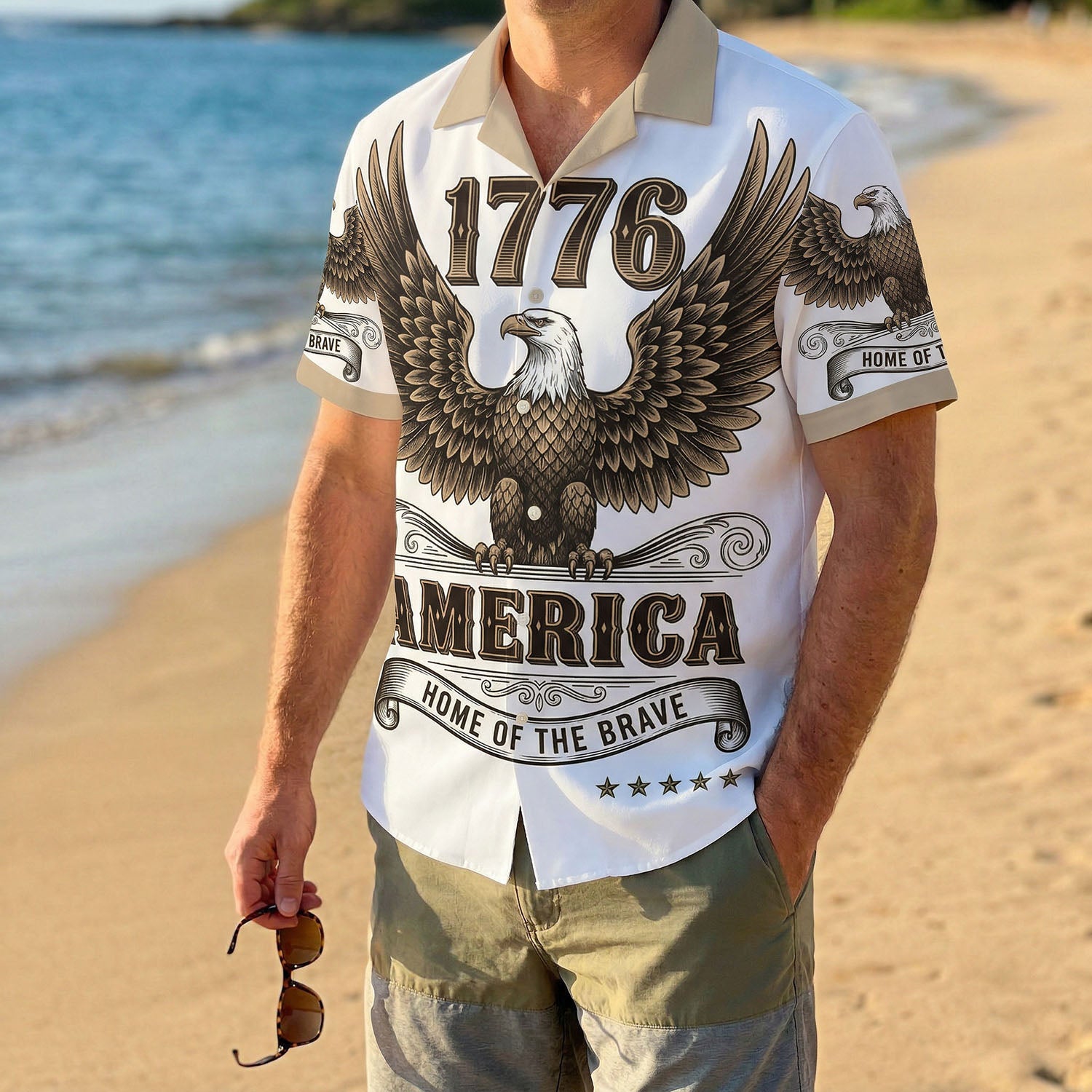 A male model wearing the 1776 America Home of the Brave Aloha shirt on a sunny beach showcasing a casual patriotic summer outfit