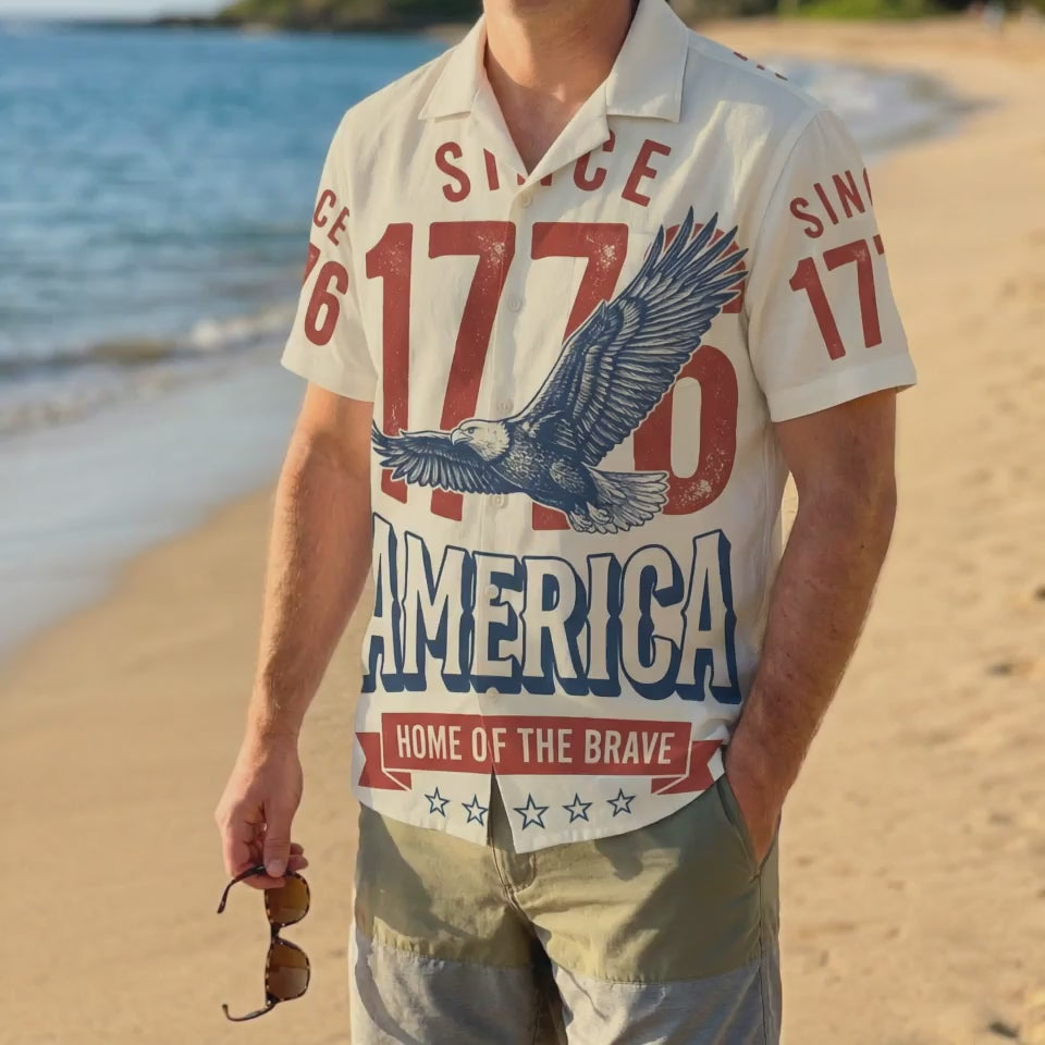 A man wearing the cream 1776 Home of the Brave shirt on a sunny beach, showcasing a relaxed patriotic summer look.