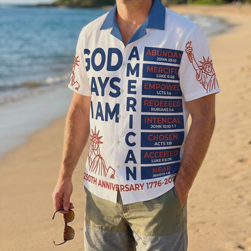 A male model wearing the white God Says I Am American religious shirt at a sunny beach showcasing a casual patriotic summer look for the 250th anniversary